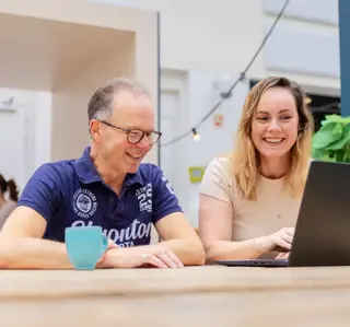 Oudere man en studente aan tafel op laptop atrium